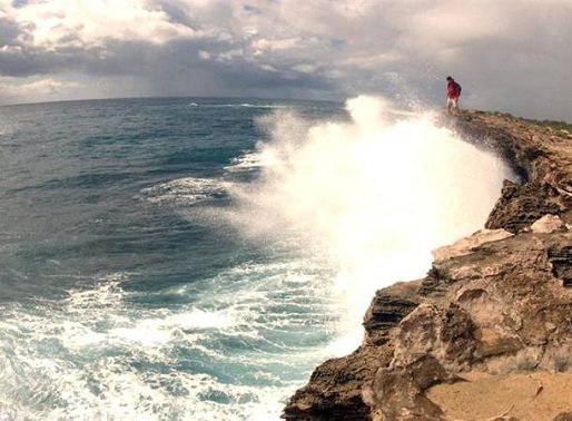 Man standing on cliff edge watching ocean waves splashing, Hawaii